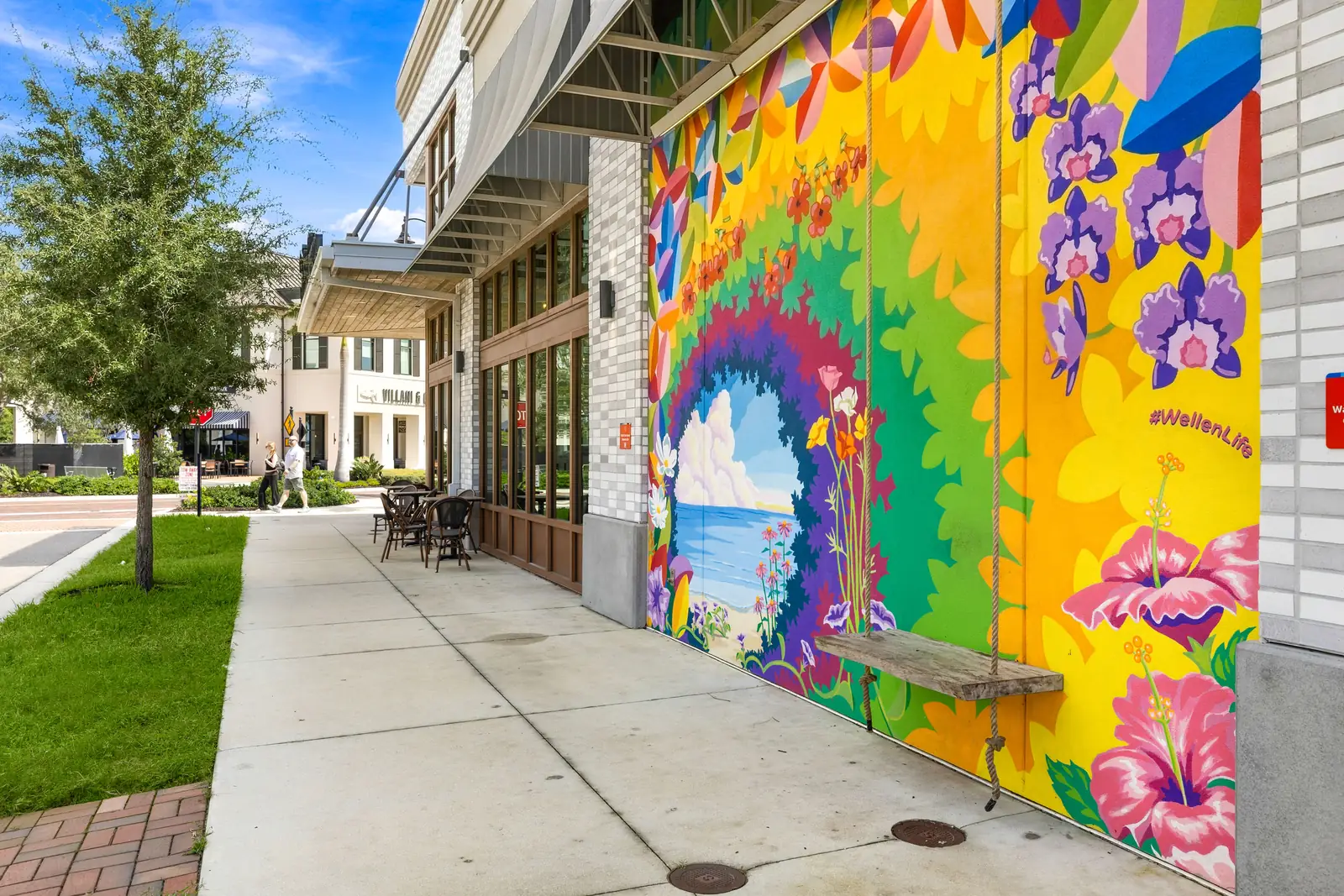 Bright floral mural with a rope swing painted on a building wall beside a sidewalk in Downtown Wellen Park